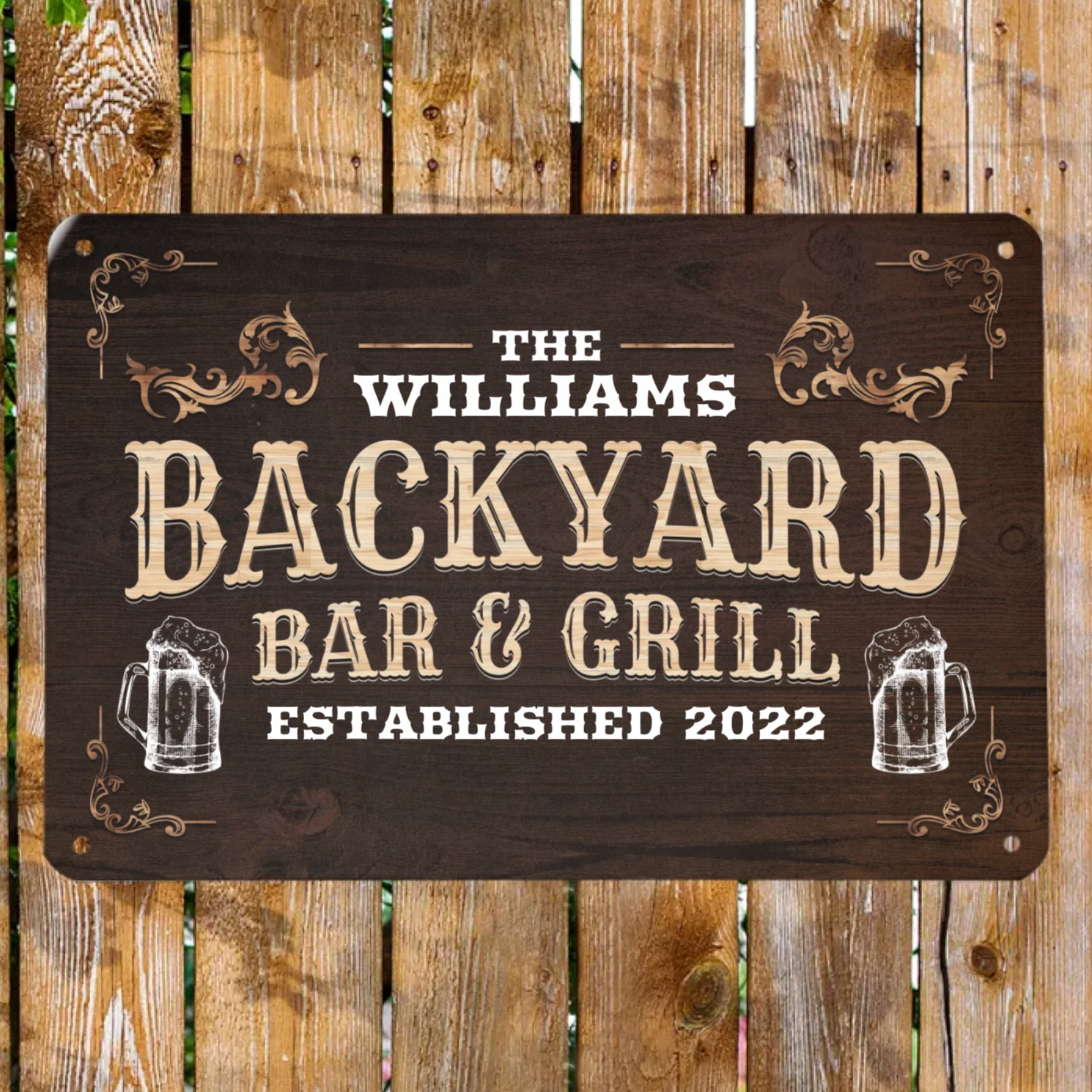 A personalized metal sign mounted on a wooden fence, reading 'The Williams Backyard Bar & Grill' with a established date below the text.